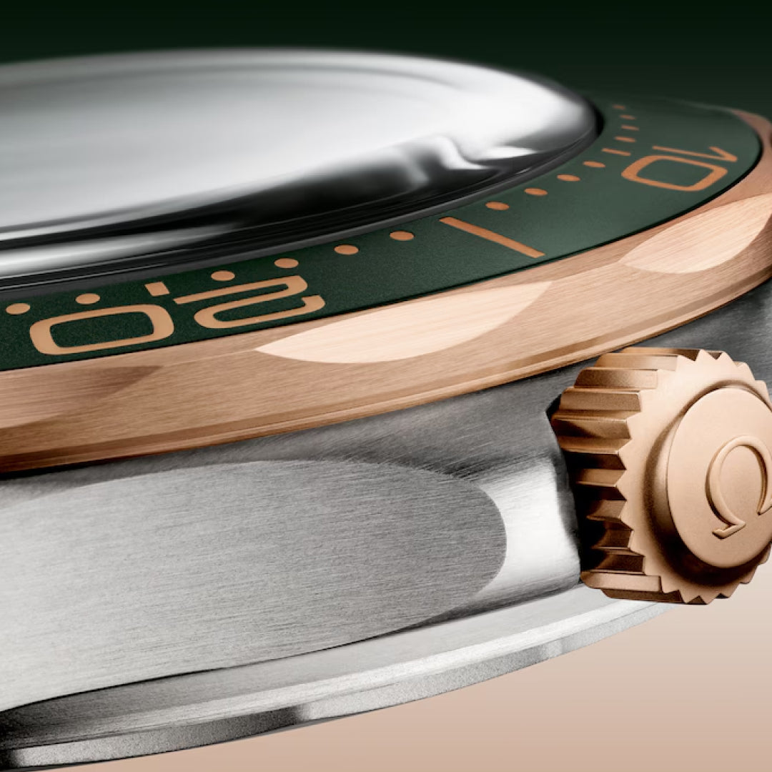Close-up of the OMEGA Seamaster Diver 300M Co-Axial Master Chronometer 42mm watch, showcasing a gold-tone ridged crown and a partially visible green bezel with gold numbering. The stainless steel case features precision movement against a dark green background.