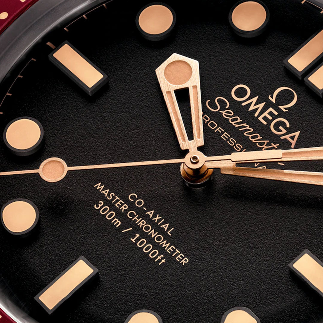 Close-up of the OMEGA Seamaster Diver 300M Co-Axial Master Chronometer 42mm watch face, featuring gold hour markers and hands, a red-tipped second hand, and text showing "Calibre 8806 300m / 1000ft" on a black background.