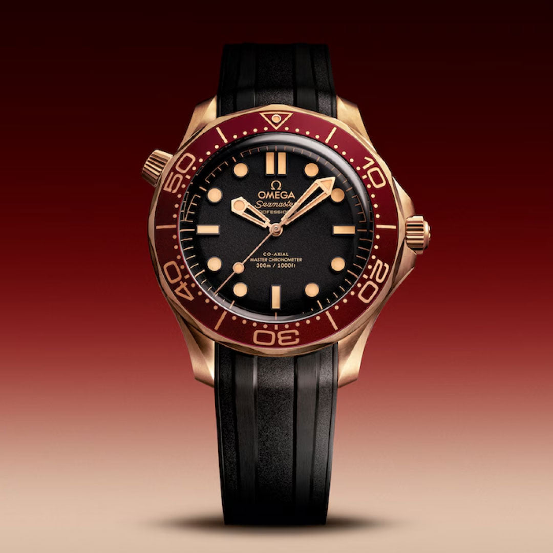 The OMEGA Seamaster Diver 300M Co-Axial Master Chronometer 42mm Watch features a black dial, gold hands, burgundy bezel, and black rubber strap—powered by the Master Chronometer Calibre 8806—displayed against a red gradient background.