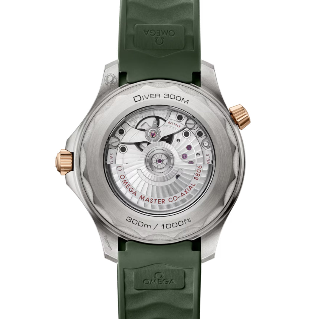 The OMEGA Seamaster Diver 300M Co-Axial Master Chronometer 42mm Watch with a green strap features a transparent case back showcasing its mechanical movement, with engravings in titanium and Bronze Gold, a gold-colored crown, "Diver 300M" marking, and water resistance up to 300m/1000ft.