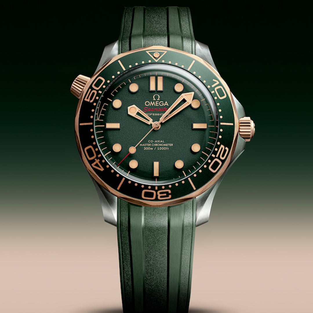 The OMEGA Seamaster Diver 300M Co-Axial Master Chronometer 42mm Watch radiates elegance with a green face and bezel, gold numerals, and a two-tone green and gold crown. Featuring the OMEGA logo on its green strap, it's crafted in titanium and Bronze Gold with the Calibre 8806 movement.
