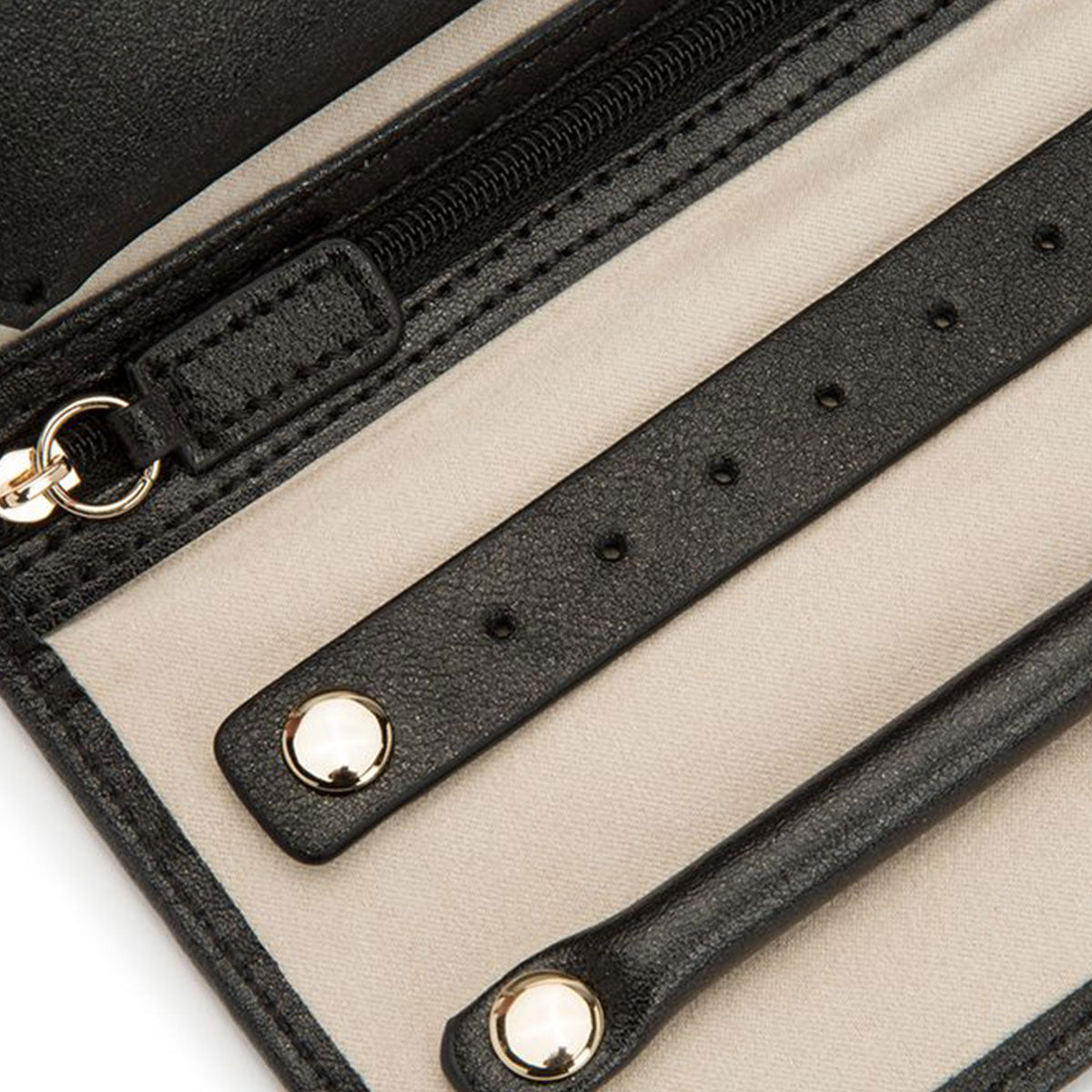 A close-up of the open WOLF 1834 Palermo Jewellery Roll highlights its elegant black leather exterior and beige anti-tarnish lining. The Palermo by WOLF features a zippered compartment, multiple card slots, and metal button closures.