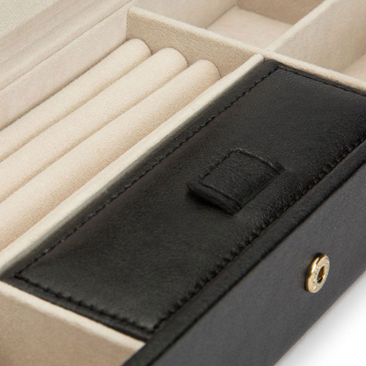 A close-up of the interior of the WOLF 1834 Palermo Safe Deposit Box showcases a black leather-covered lid with a reliable snap closure. It features multiple cushioned slots for rings and various compartments for accessories, all lined with LusterLoc anti-tarnish beige fabric to safeguard your cherished items.