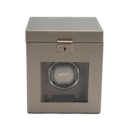 The WOLF 1834 Palermo Single Watch Winder with Jewelry Storage is a sophisticated accessory, featuring a gray, square design with a transparent front that displays one slot. It bears the WOLF branding and includes a metallic lock at the center top. The contemporary, sleek look includes rotation settings for customization and exudes a smooth texture.