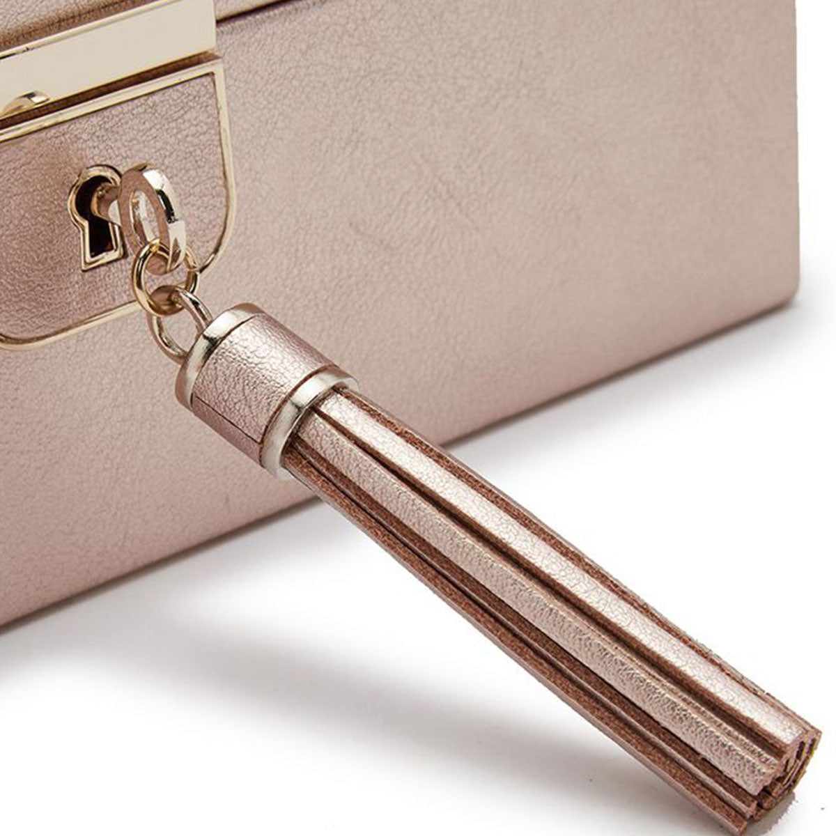 A close-up of a rose gold leather tassel keychain attached to the WOLF 1834 Palermo 6 Piece Watch Box by WOLF. The tassel elegantly hangs, accentuating its color and texture against the smooth surface of the watch box's compartments.