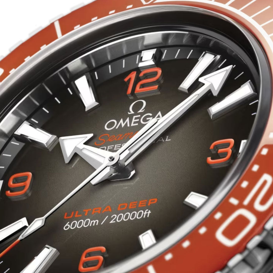 Close-up of an OMEGA Seamaster Planet Ocean 6000M Ultra Deep Co-Axial Master Chronometer 45.5mm watch face showcasing bold, silver hands and orange accents. This water-resistant masterpiece features a depth rating of 6000m/20000ft and a distinctive rotating bezel in orange, with "Ultra Deep" proudly displayed on its elegant black dial.