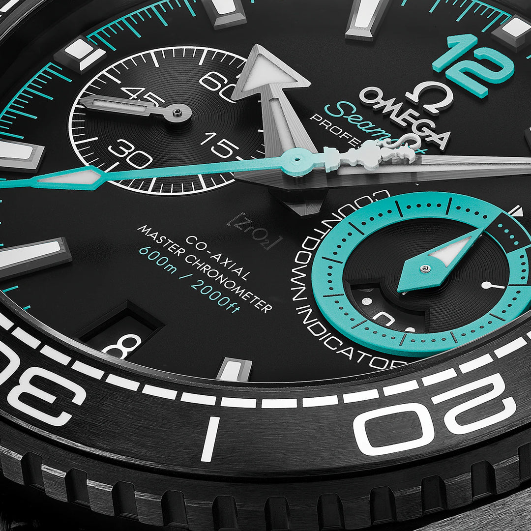 Close-up of the OMEGA Seamaster Planet Ocean 600M Co-Axial Master Chronometer Chronograph 45.5mm watch face, highlighting intricate details such as a turquoise second hand and chronograph sub-dials, taking inspiration from America's Cup. With its black dial and white and turquoise accents, this timepiece features a ceramic bezel and a black ceramic case.