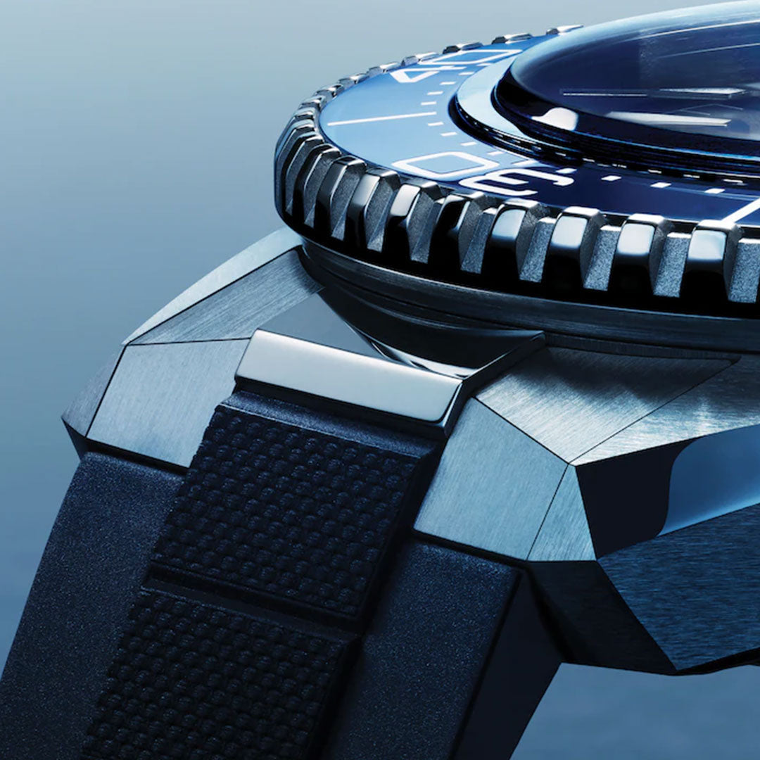 Close-up of the OMEGA Seamaster Planet Ocean 600M Co-Axial Master Chronometer 42mm Watch, showcasing its metallic bezel, textured rubber strap, and polished case craftsmanship against a blue gradient background.