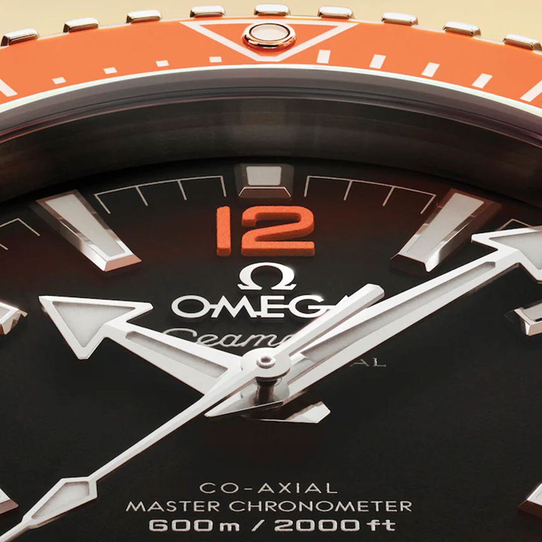 Close-up of the OMEGA Seamaster Planet Ocean 600M Co-Axial Master Chronometer 42mm Watch shows bold white hands, orange 12 numeral, “Co-Axial Master Chronometer 600m/2000ft” text, and an orange bezel at the top.