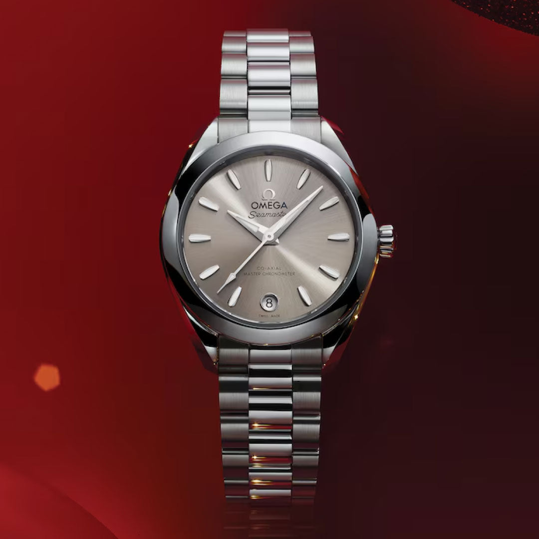 The OMEGA Seamaster Aqua Terra 150M Co-Axial Master Chronometer 30mm Watch, featuring a stainless steel band and beige dial with silver hour markers and a date window at 6 o’clock, is displayed against a red gradient background.