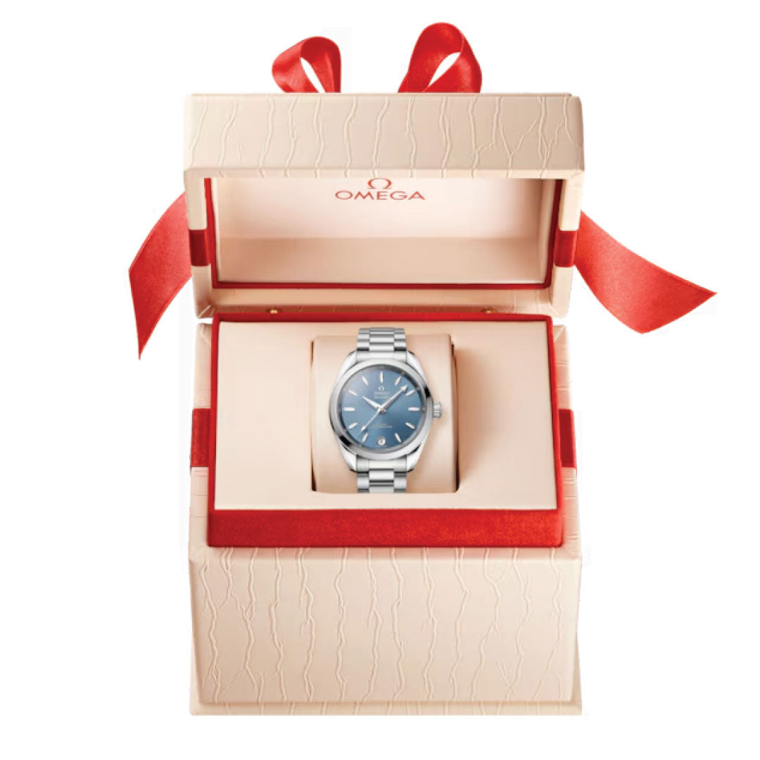 A silver OMEGA Seamaster Aqua Terra Shades Co-Axial Master Chronometer 34mm watch featuring a blue face is elegantly displayed inside an open beige gift box adorned with a red ribbon. The inside of the box lid is graced by the OMEGA logo, underscoring the precision of its Master Chronometer calibre 8800.