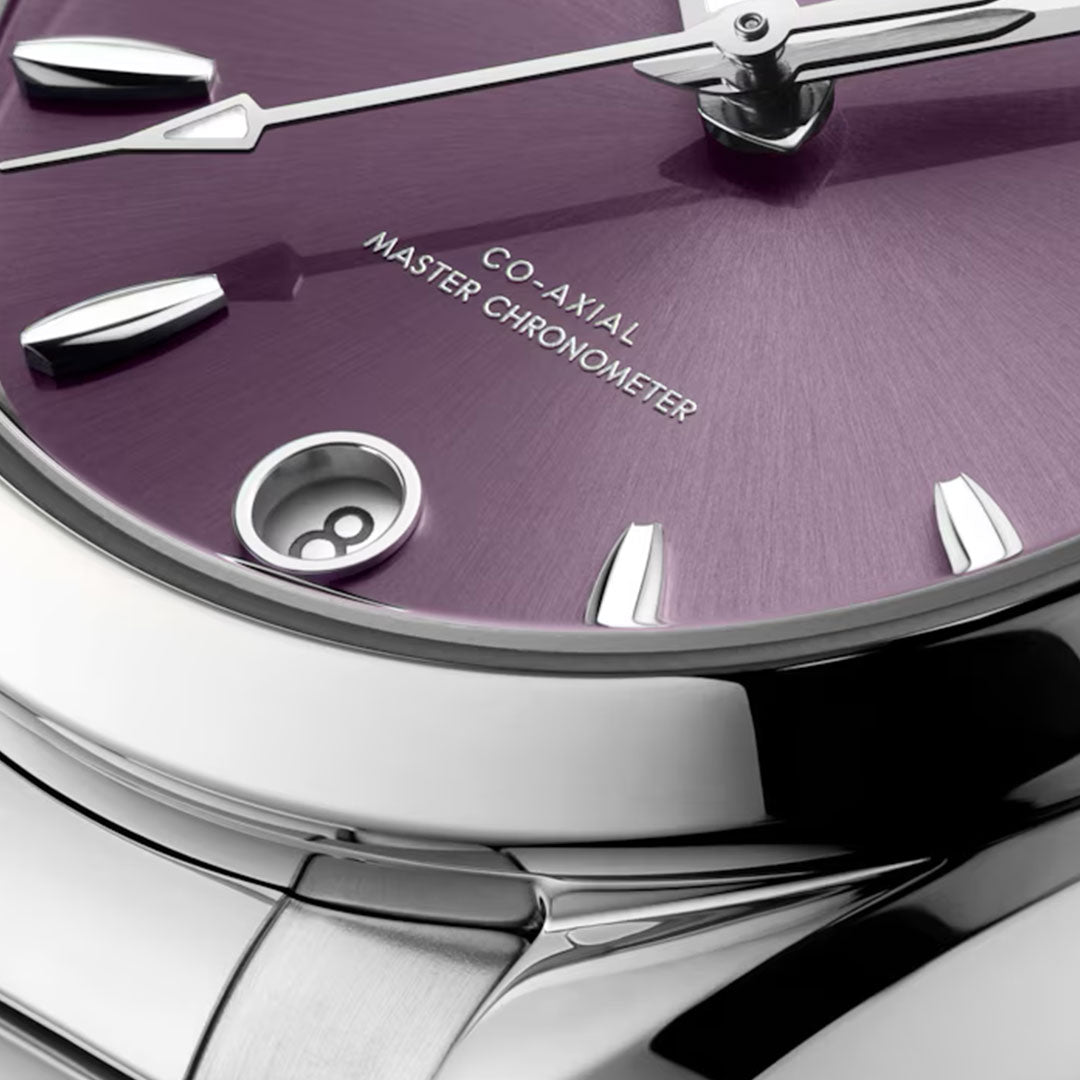 Close-up of the OMEGA Seamaster Aqua Terra Shades Co-Axial Master Chronometer 34mm watch, featuring a purple dial, silver markers and hands, “CO-AXIAL MASTER CHRONOMETER” text, date at 8 o’clock, and a polished metal bracelet and case.