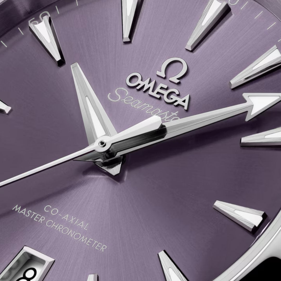 A close-up of the OMEGA Seamaster Aqua Terra Shades Co-Axial Master Chronometer 38mm watch shows a metallic purple dial with silver hour markers, hands, visible branding, and a date window displaying the number 8.
