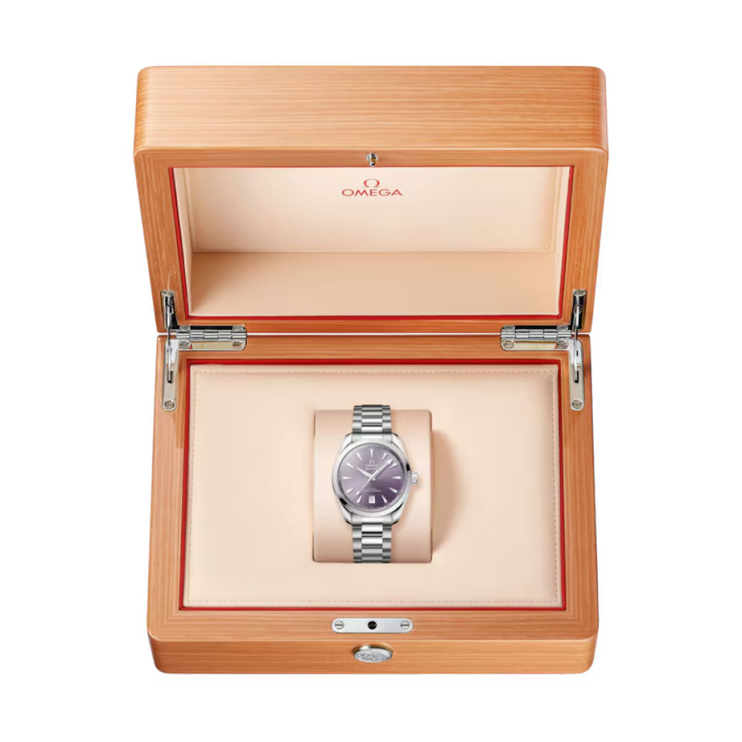 A silver OMEGA Seamaster Aqua Terra Shades Co-Axial Master Chronometer 38mm Watch with a purple face is displayed in an open wooden box lined with beige and red, highlighting the collection’s refined elegance.