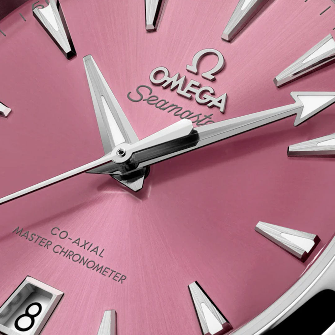 Close-up of an OMEGA Seamaster Aqua Terra Shades Co-Axial Master Chronometer 38mm watch face in pink, featuring silver hour markers, hands, logo, and a date window at 6 o’clock with “CO-AXIAL MASTER CHRONOMETER” text.