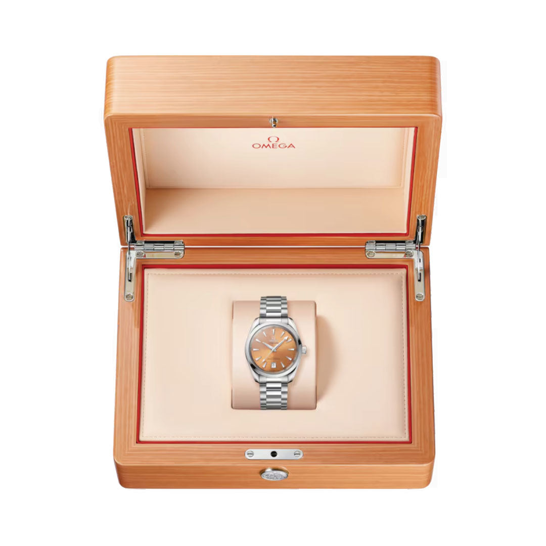 The OMEGA Seamaster Aqua Terra Shades Co-Axial Master Chronometer 38mm Watch, crafted in silver with an orange dial, is elegantly presented in an open wooden box featuring a beige interior. The Omega logo on the box lid highlights its Seamaster Aqua Terra heritage and OMEGA's maritime legacy. This Co-Axial Master Chronometer embodies both precision and elegance.