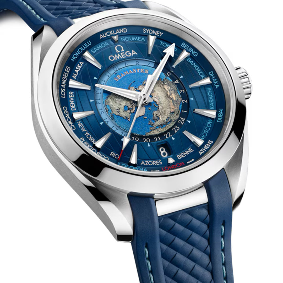 The OMEGA Seamaster Aqua Terra 150M Worldtimer Co-Axial Master Chronometer 43mm features a blue textured strap, detailed blue dial with Worldtimer for various time zones, and a central world map. Encased in stainless steel, it runs on the Master Chronometer Calibre 8938.