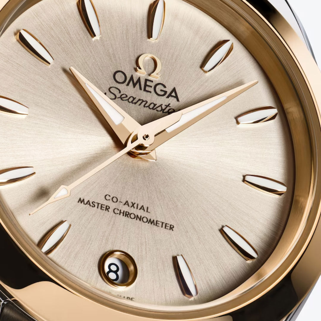 Close-up of the OMEGA Seamaster Aqua Terra 150M Co-Axial Master Chronometer 30mm Watch with a champagne dial, gold hour markers and hands in 18K Moonshine Gold, and a date window at 6 o’clock. The dial reads “Co-Axial Master Chronometer.”.