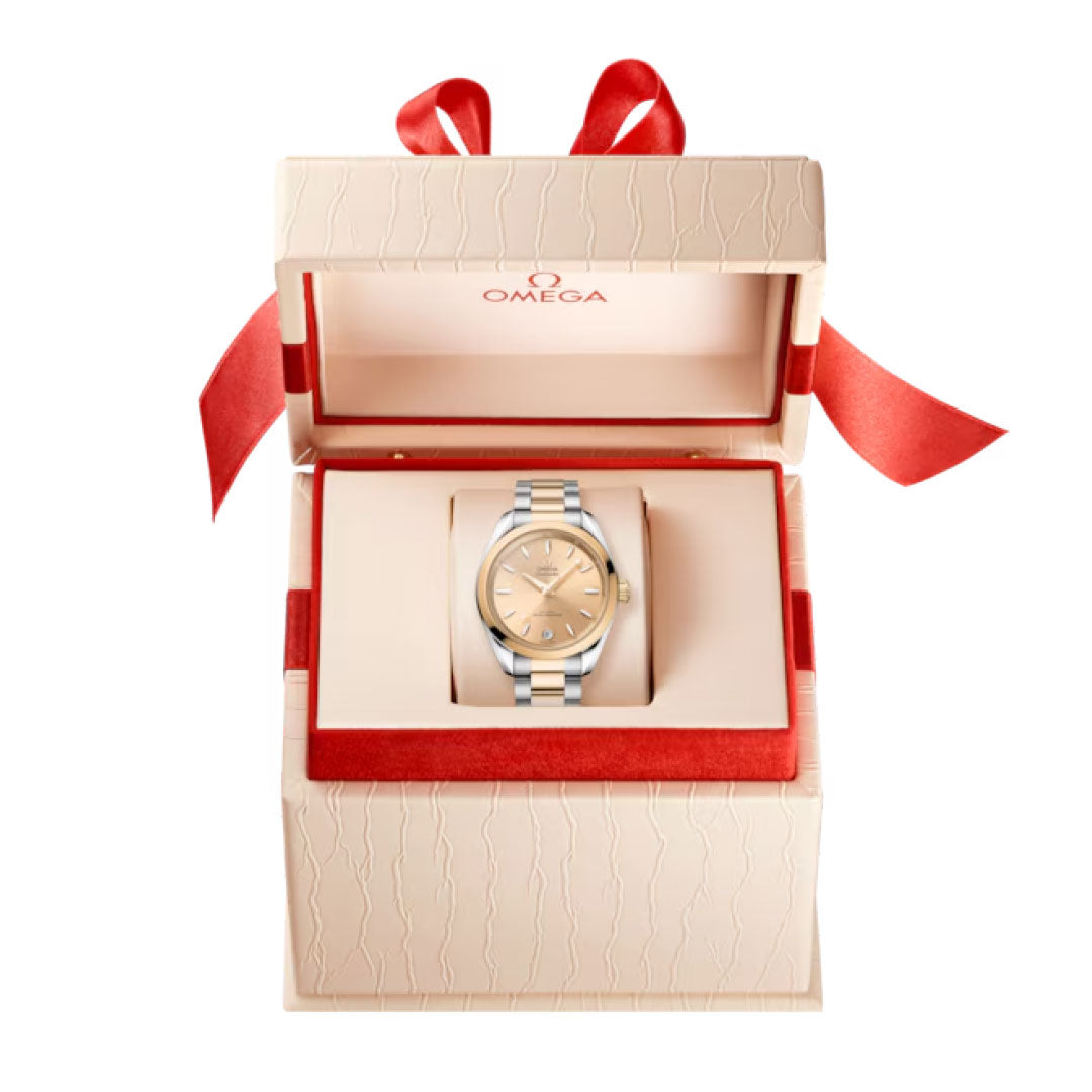 The OMEGA Seamaster Aqua Terra Shades Co-Axial Master Chronometer 34mm Watch is presented in a cream-colored box with red ribbon and trim, featuring the embossed OMEGA logo and showcasing the Seamaster Aqua Terra collection.