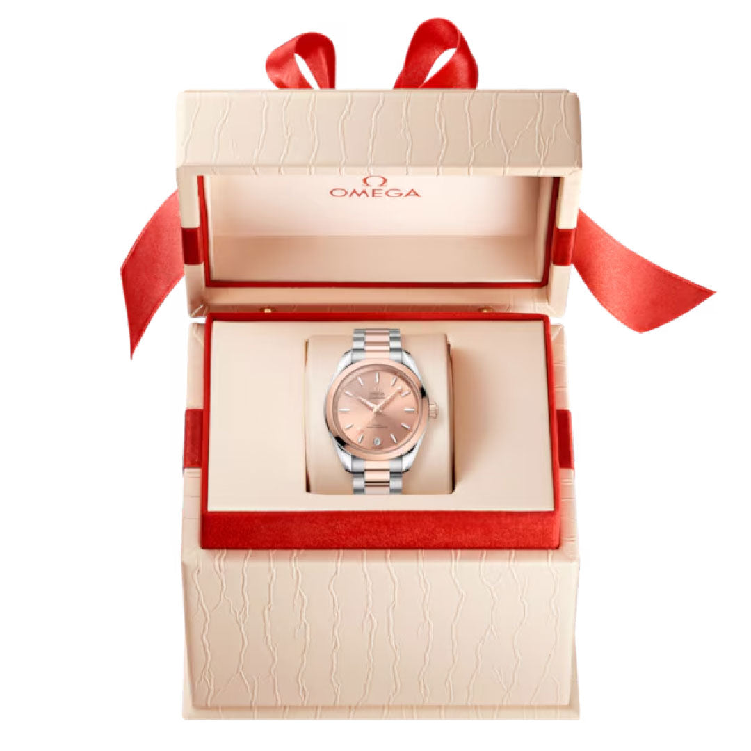 An OMEGA Seamaster Aqua Terra Shades Co-Axial Master Chronometer 34mm watch with a rose gold dial, presented in an open cream gift box lined with red velvet and topped with a red ribbon bow.