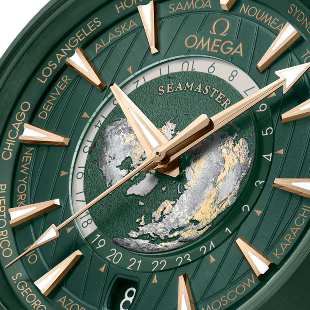 A close-up of the OMEGA Seamaster Aqua Terra 150M Worldtimer Co-Axial Master Chronometer 43mm Watch reveals its green and gold design, stainless steel accents, multiple time zones on the edge, a world map on the face, and prominent gold hour markers with "Seamaster" clearly displayed.
