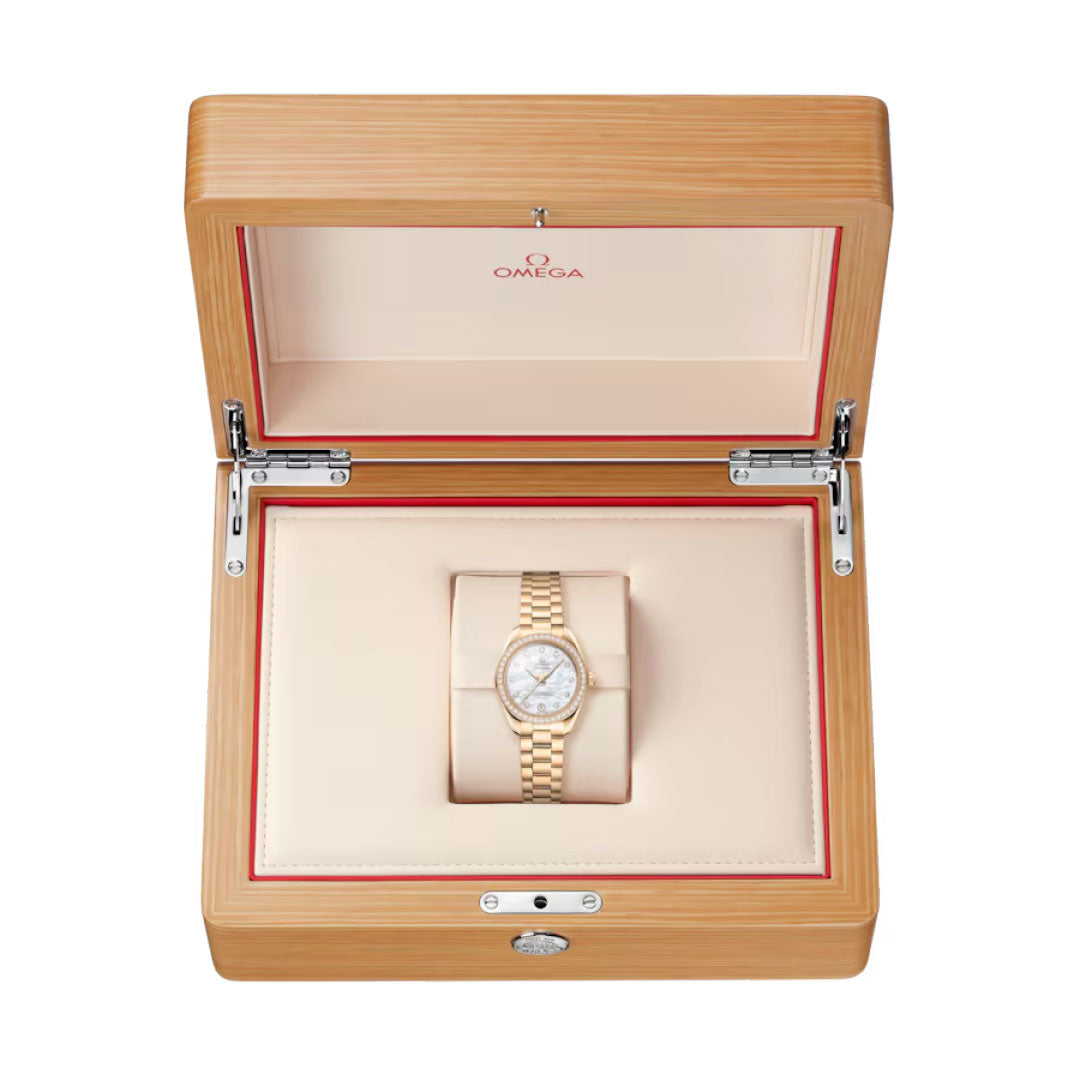 An OMEGA Seamaster Aqua Terra 150M Co-Axial Master Chronometer 30mm watch with a gold case and white dial is showcased in an open light wood OMEGA box featuring beige and red interior lining.