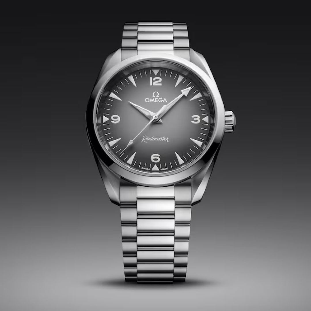 The OMEGA Seamaster Railmaster Co-Axial Master Chronometer 38mm features a black dial, silver hour markers, and a stainless steel bracelet, showcased against a gray gradient background.