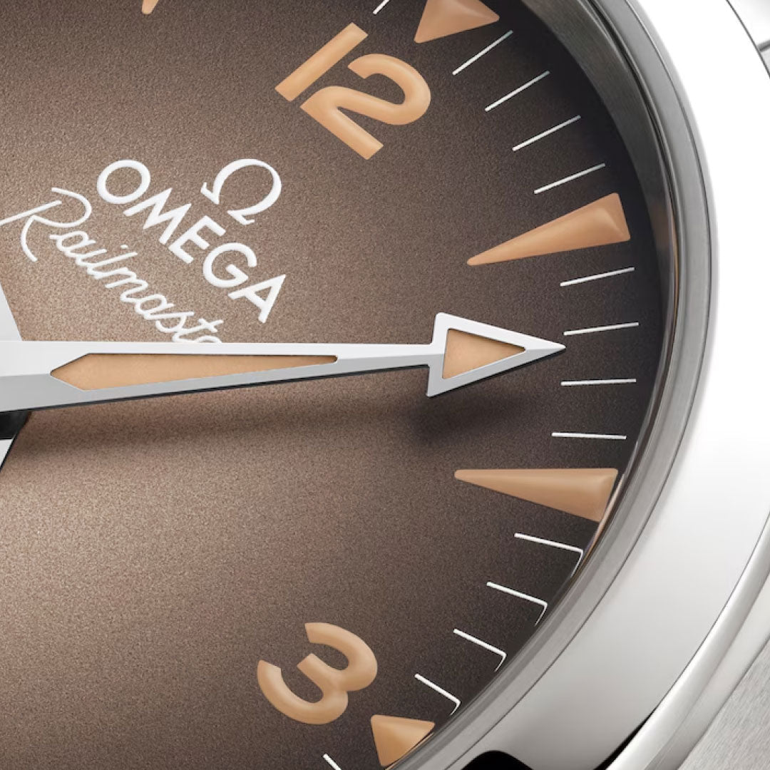 Close-up of the OMEGA Seamaster Railmaster Co-Axial Master Chronometer 38mm Watch shows a brown gradient dial with cream numerals and hands, precision powered by Calibre 8804, and a glimpse of the silver case edge on the right.