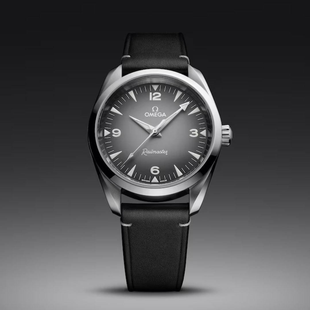 The OMEGA Seamaster Railmaster Co-Axial Master Chronometer 38mm Watch features a black leather strap, gray dial, silver hour markers, and white accents. This luxury OMEGA timepiece is set against a dark gradient background.