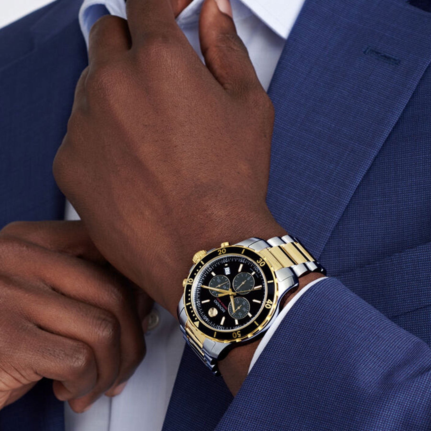 A person in a blue suit adjusts their collar, drawing attention to the Movado Series 800 Quartz 42mm watch, featuring a stylish silver and gold band and an elegant chronograph dial.