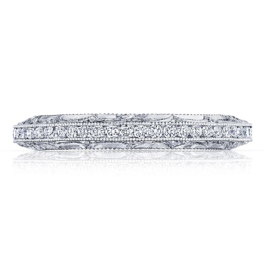 A close-up of the Tacori Reverse Crescent Platinum Round Brilliant Anniversary Ring showcases a band of small, sparkling diamonds. This Tacori ring features intricate engravings along the sides, enhancing its elegant and detailed appearance against a plain white surface.