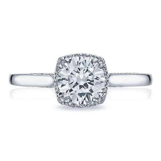 The Tacori Dantela 18K White Gold Round Brilliant Semi Mount Engagement Ring exemplifies the timeless beauty of engagement rings with its prominent round diamond in a prong setting, adorned by a hidden square halo of smaller diamonds. Resting on a slim band, this exquisite piece is elegantly displayed against a white background.