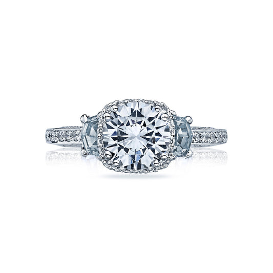 Presenting the Tacori Dantela 18K White Gold Round Brilliant Semi Mount Three Stone Hidden Halo Engagement Ring with Diamond Band and Side Stone by Tacori. This stunning piece showcases a prominent round-cut diamond at its center, enhanced by a halo of smaller diamonds. Trapezoidal gems complement each side, while additional diamonds grace the band. To elevate its elegance, the design is further beautified with half-moon sapphires.