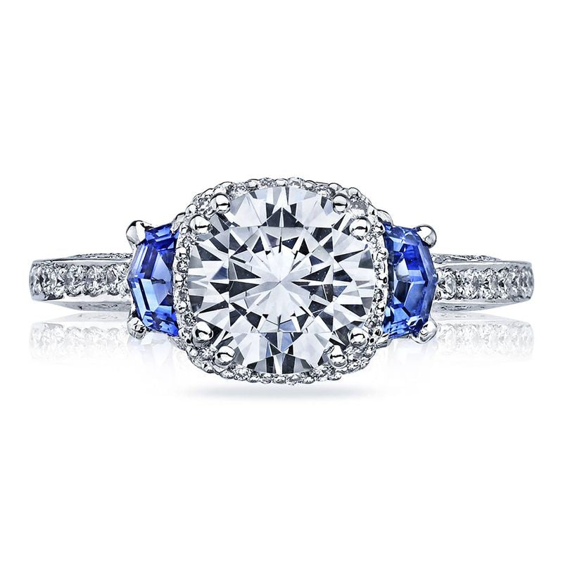The Tacori Dantela 18K White Gold Round Brilliant Semi Mount Three Stone Hidden Halo Engagement Ring showcases a large central round diamond, flanked by two elegant oval sapphire side stones. The diamond band adds an extra touch of sparkle and sophistication to this stunning design.