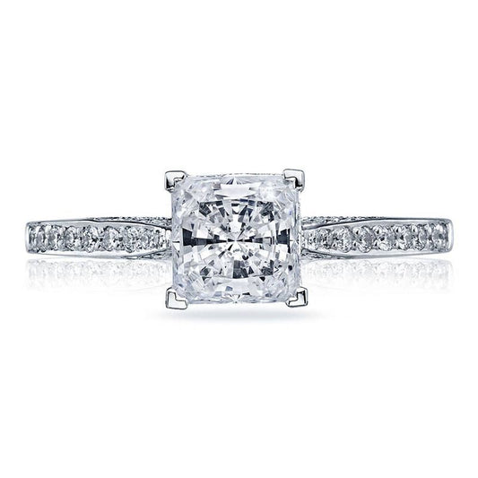 The Tacori Dantela Platinum Princess Cut Semi Mount Solitaire Engagement Ring with Diamond Band by Tacori showcases a stunning square diamond in the center, secured by four prongs. Its band is adorned with smaller diamonds, offering an elegant and reflective setting that enhances the brilliance of these exquisite gems.