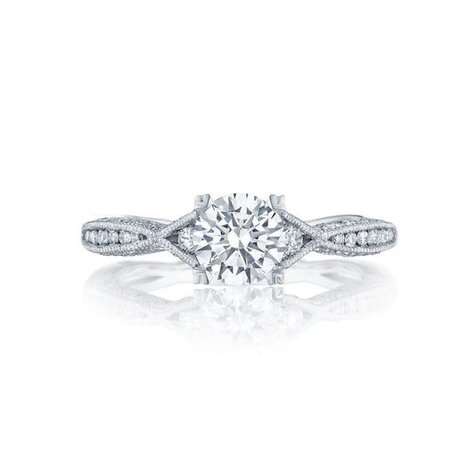The Tacori Classic Crescent 18K White Gold Round Brilliant Semi Mount Solitaire Engagement Ring with Diamond Band showcases a central round diamond. The band is intricately designed with an intertwined pattern and adorned with smaller diamonds along the sides, set against a white background.