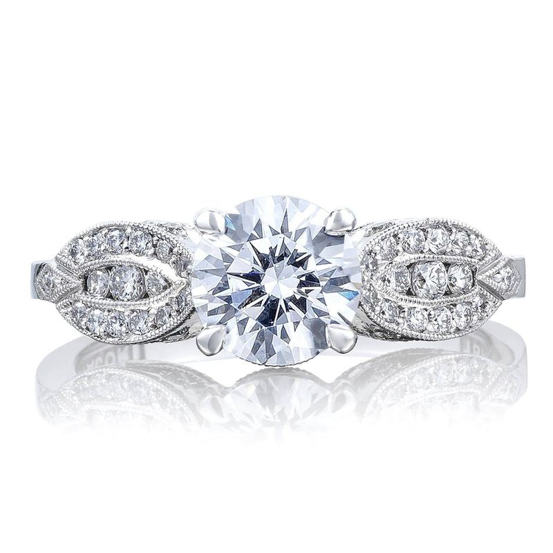 Introducing the Tacori Simply 18K White Gold Round Brilliant Semi Mount Solitaire Engagement Ring with a Diamond Band. This sophisticated Tacori engagement ring showcases an impressive round center diamond, enhanced by its detailed craftsmanship and a band adorned with exquisite pave-set diamonds that reflect its brilliance.