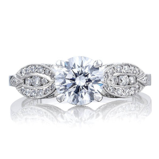 Introducing the Tacori Simply 18K White Gold Round Brilliant Semi Mount Solitaire Engagement Ring with a Diamond Band. This sophisticated Tacori engagement ring showcases an impressive round center diamond, enhanced by its detailed craftsmanship and a band adorned with exquisite pave-set diamonds that reflect its brilliance.