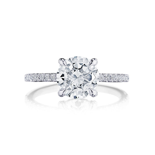 The Tacori Simply 18K White Gold Round Brilliant Semi Mount with Diamond Band and Hidden Halo Engagement Ring is beautifully highlighted in a close-up view. It features a prominent round diamond centerpiece, accompanied by pavé-set diamonds on the band that enhance its elegant and sparkling appearance. Expertly crafted by Tacori gemologists, this exquisite piece is set against a white background.