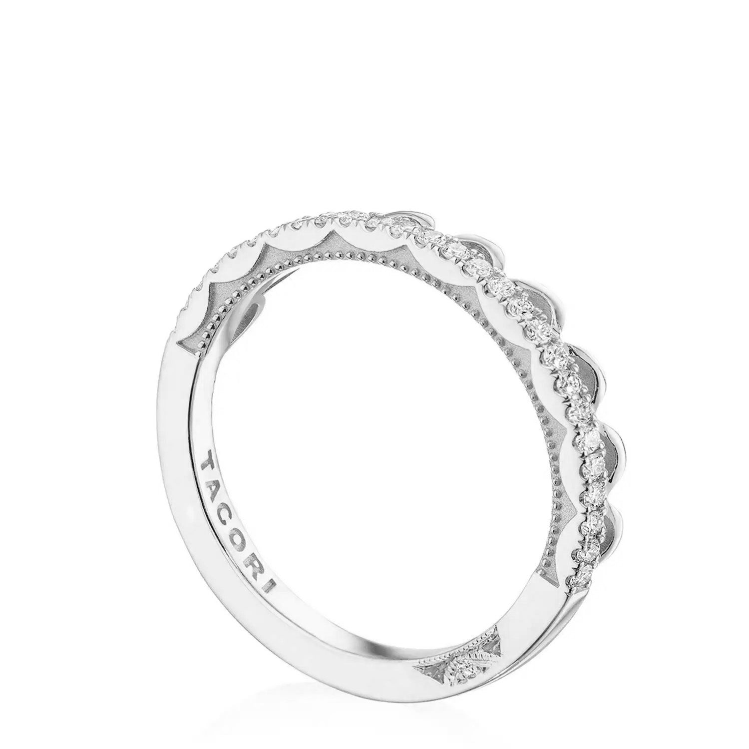 A Tacori Crescent Crown 18K white gold anniversary ring displays intricate detailing along its outer edge, featuring small round-brilliant diamonds arranged in a scalloped pattern. Inside, the band is engraved with the brand name "Tacori.