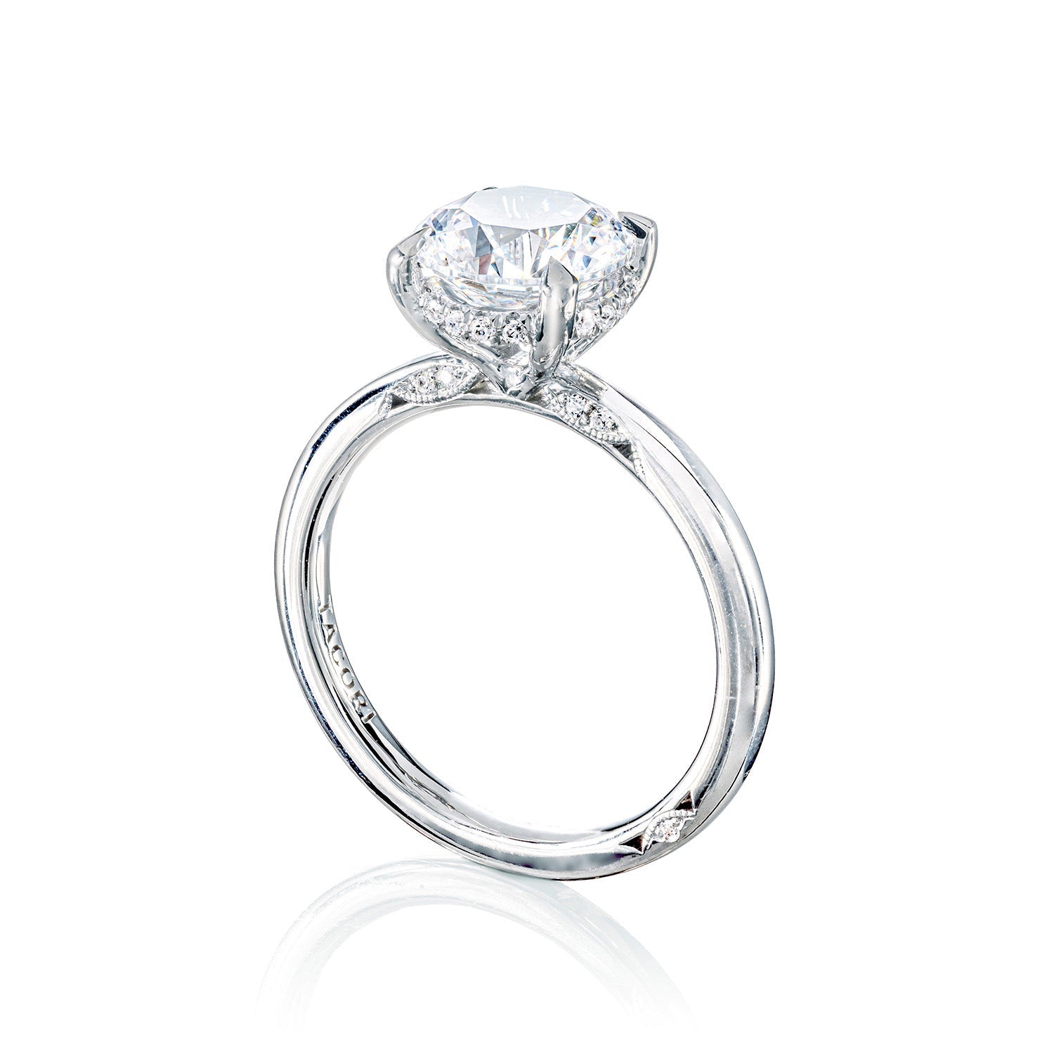 The Tacori Simply 18K White Gold Round Brilliant Solitaire Semi Mount Engagement Ring, featuring a stunning round diamond centerpiece, is complemented by a band with subtle diamond accents. Presented on a reflective surface against a white backdrop, this refined piece embodies timeless elegance and the lasting allure of diamonds.