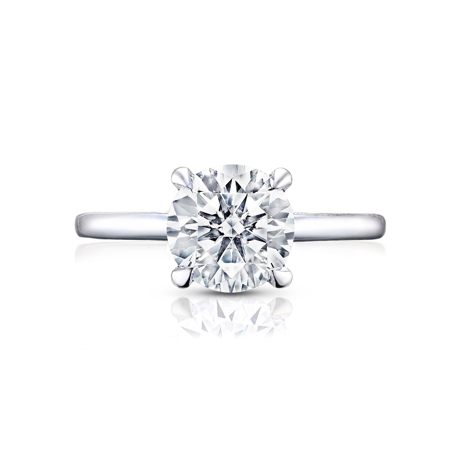 A Tacori Simply engagement ring, crafted from 18K white gold, features a single large round brilliant diamond in a four-prong setting. The smooth and polished band elegantly reflects light and includes diamond accents. Centered on a white background, this exquisite piece by Tacori highlights the elegance and simplicity characteristic of premium engagement rings.