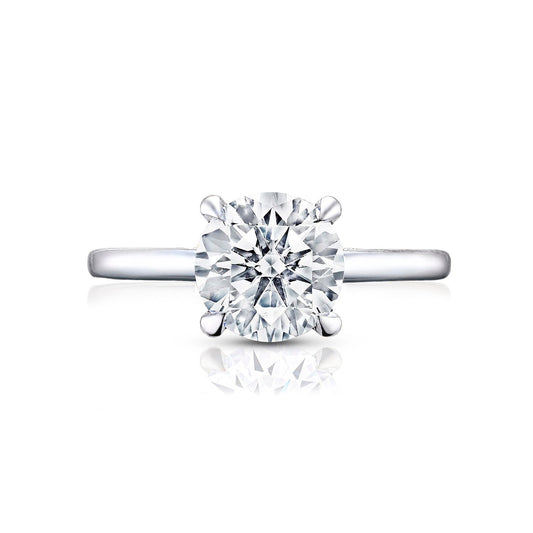A Tacori Simply engagement ring, crafted from 18K white gold, features a single large round brilliant diamond in a four-prong setting. The smooth and polished band elegantly reflects light and includes diamond accents. Centered on a white background, this exquisite piece by Tacori highlights the elegance and simplicity characteristic of premium engagement rings.