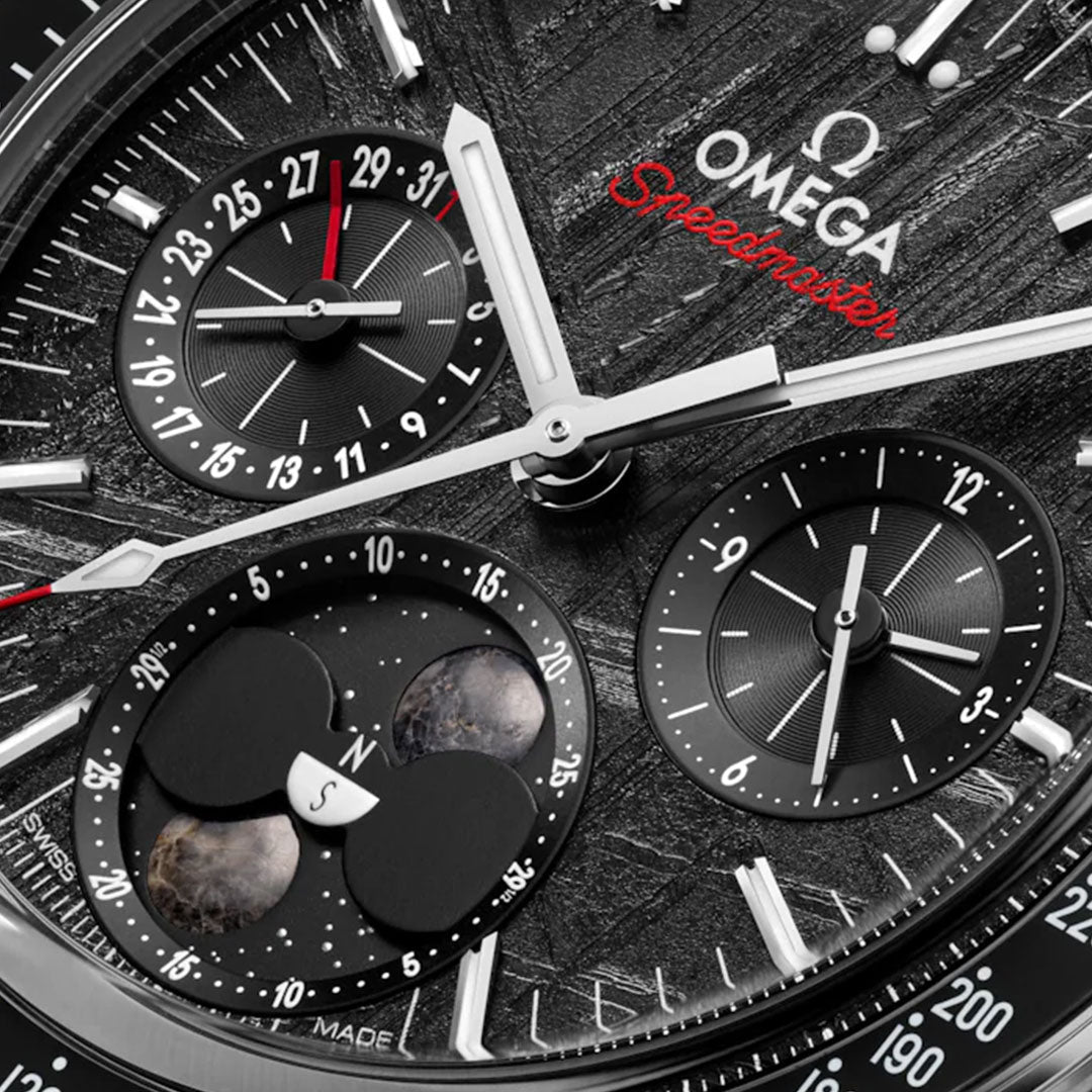 Close-up of the OMEGA Speedmaster Moonphase Co-Axial Master Chronometer Chronograph 43mm watch, featuring a moon phase display, date subdial, chronograph functions, and meteorite dial on a textured black background with silver markers and hands.