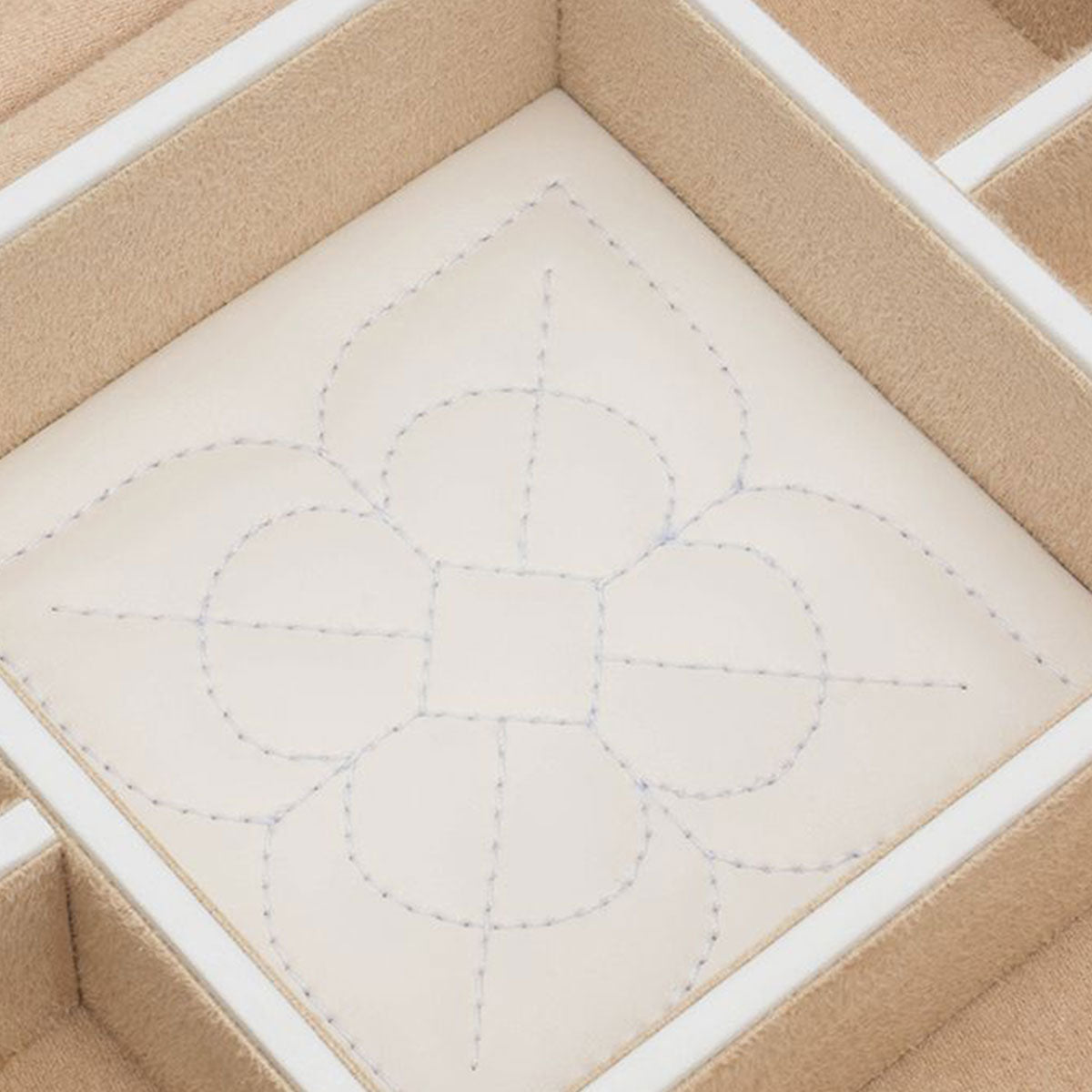 Close-up of a beige fabric with a stitched symmetrical pattern resembling a flower or geometric design, placed inside the WOLF 1834 Marrakesh Cream Jewellery Box, showcasing WOLF's LusterLoc™ technology.