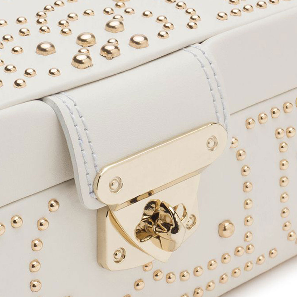 A close-up view of the WOLF 1834 Marrakesh Cream Jewellery Box showcases its white leather adorned with gold studs and a gold clasp. These studs create decorative patterns on the surface, giving it a luxurious feel similar to a gold-studded jewelry box.