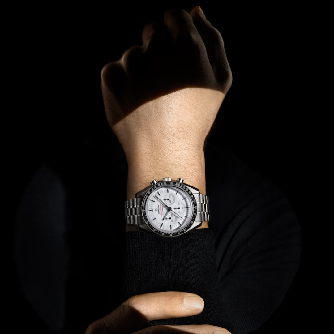 A person wearing the OMEGA Speedmaster Moonwatch Professional Co-Axial Master Chronometer 42mm holds their arm upright against a black background, dramatic shadows highlighting the iconic OMEGA chronograph design.