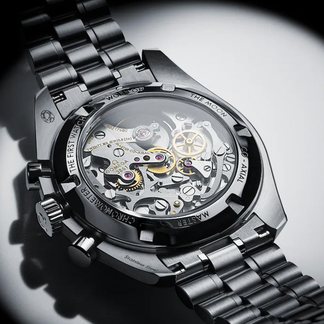 A close-up of the transparent case back on the OMEGA Speedmaster Moonwatch Professional Co-Axial Master Chronometer Chronograph 42mm Watch reveals its intricate movement, with engravings around the stainless steel edge highlighting achievements and model details.