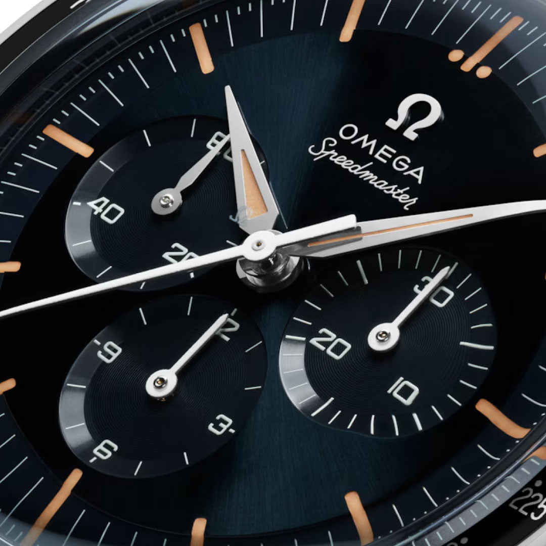 Close-up of the OMEGA Speedmaster First OMEGA in Space Co-Axial Master Chronometer 39.7mm watch face, featuring three subdials, white markings, orange-accented hands, and the OMEGA logo with "Speedmaster" on a dark blue background.