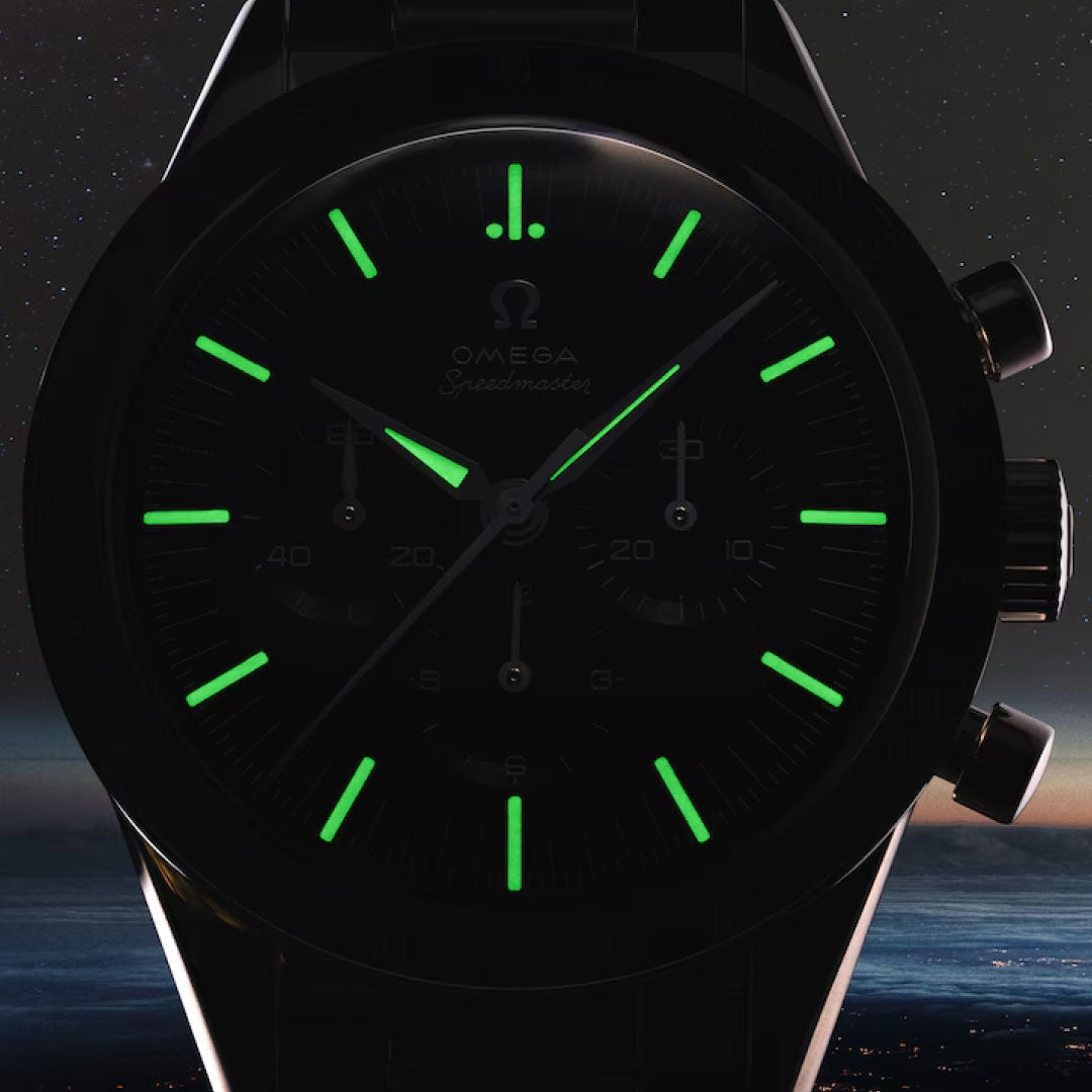A close-up of the OMEGA Speedmaster First OMEGA in Space Co-Axial Master Chronometer 39.7mm Watch, with green luminescent hour markers and hands glowing against a dim, star-studded night sky.